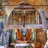 Wnętrze drewnianego kościoła z łukiem arkady belki tęczowej z krucyfiksem i figurami świętych.