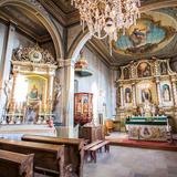 Wnętrze drewnianego kościoła. Nawa główna i boczna oraz prezbiterium, ławy, ołtarze bogato zdobione i filary z arkadami.