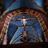 Zbliżenie na belkę przy prezbiterium z dużym krzyżem z ukrzyżowanym Chrystusem. Nad nim łuk i sklepienie kolebkowe sufitu malowanego w gwiazdy na niebieskim tle nieba.