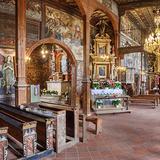 Bogato zdobione wnętrze drewnianego kościoła z ołtarzem głównymi bocznym. Po lewej stronie drewniane zdobione ławki. Na ścianach i suficie malowidła.
