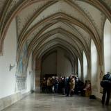 Pomieszczenie klasztorne, długi korytarz z freskami na sklepieniu żebrowym, z białymi ścianami. Po lewej na ścianie malowidło a po prawej okna z łukiem. Na końcu korytarza turyści.