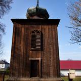Drewniana dzwonnica na kamiennej podmurówce z hełmem.