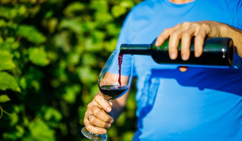 Muž nalievajúci víno do pohára v pozadí viničového kríka