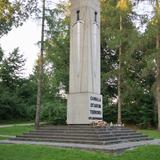 Fragment lasu. W nim Obelisk ze zniczem na szczycie i tablicą pamiątkową.