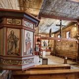 Wnętrze kościoła. Drewniana ambona z wizerunkami Ewangelistów, w tle ołtarz główny, ściany i sufit pokryte malowidłami w odcieniach brązu.