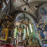 Wnętrze kościoła. Bogato zdobione ciemne ołtarze ze złotymi elementami. Malowidła na suficie i ścianach.