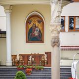 Obraz Matki Boskiej na ścianie kościoła na dziedzińcu klasztornym. Pod nim stół oraz kilka krzeseł. Przed budynkiem kolumna z rzeźbą Matki Boskiej.