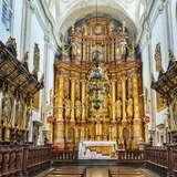 Wnętrze kościoła. Złoty, bardzo wysoki i bogato zdobiony ołtarz główny. Po obu stronach przed ołtarzem znajdują się drewniane wysokie ławki.