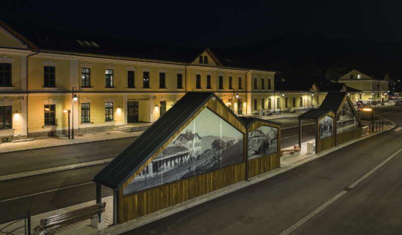 Widok na Centrum Komunikacyjne w Zakopanem nocą. Na pierwszym planie przystanki autobusowe ozdobione historycznymi fotografiami. W tle budynki Centrum Komunikacyjnego.