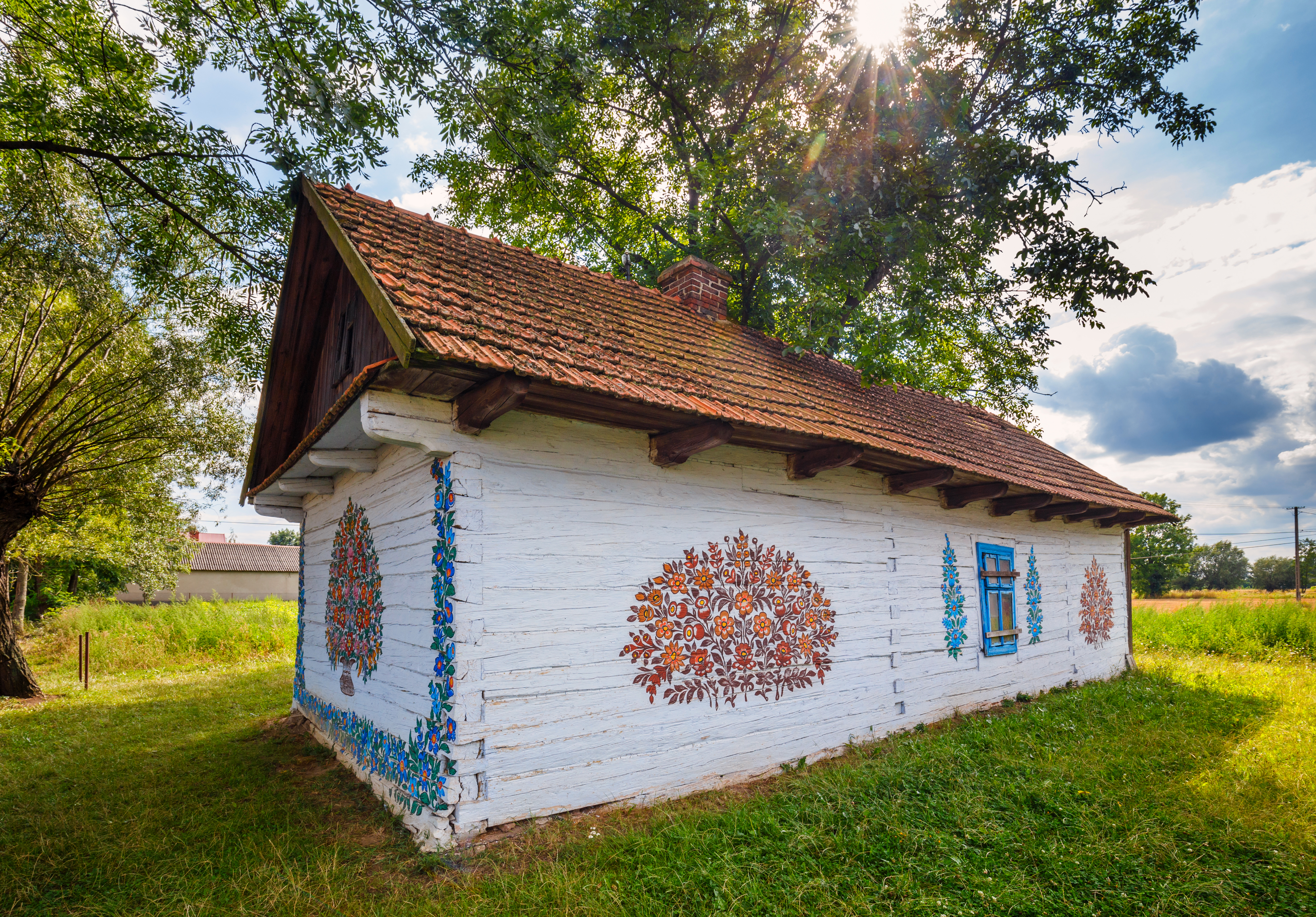 Biała chata z wymalowanym na ścianach kolorowym bukietem.